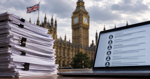 A stack of consultation documents and a laptop displaying digital submissions, with the Houses of Parliament and a Union Jack in the background.