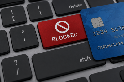 Blue credit card beside a red “Blocked” key on a computer keyboard.