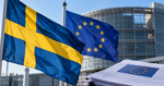 Swedish and European Union flags outside a European institutional building, illustrating uncertainty over proposed EU nicotine taxes.